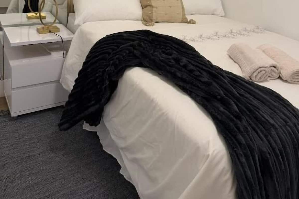 A hotel room with a bed, bedside table, lamp, and a wardrobe.