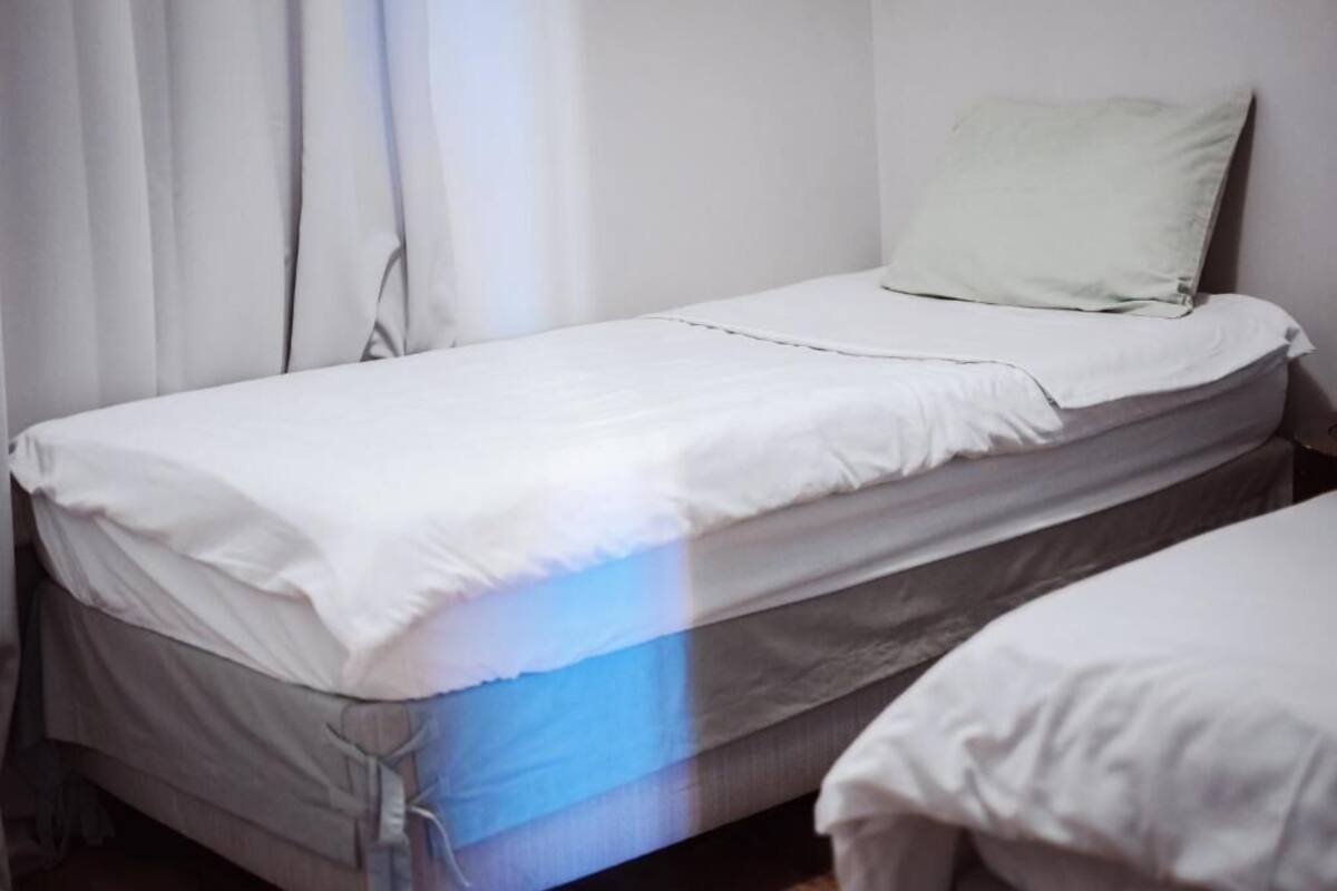 A single bed with white bedding and a pillow in a room with white walls and curtains.