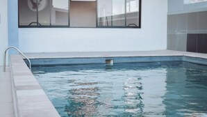 A swimming pool with a metal ladder, a tiled deck, and a window with blinds. - 77 on Independence Apartments (Windhoek)