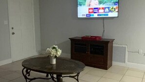 Una sala de estar con un televisor de pantalla plana montado en la pared, una mesa redonda de centro con un jarrón de flores y un sofá de cuero marrón.