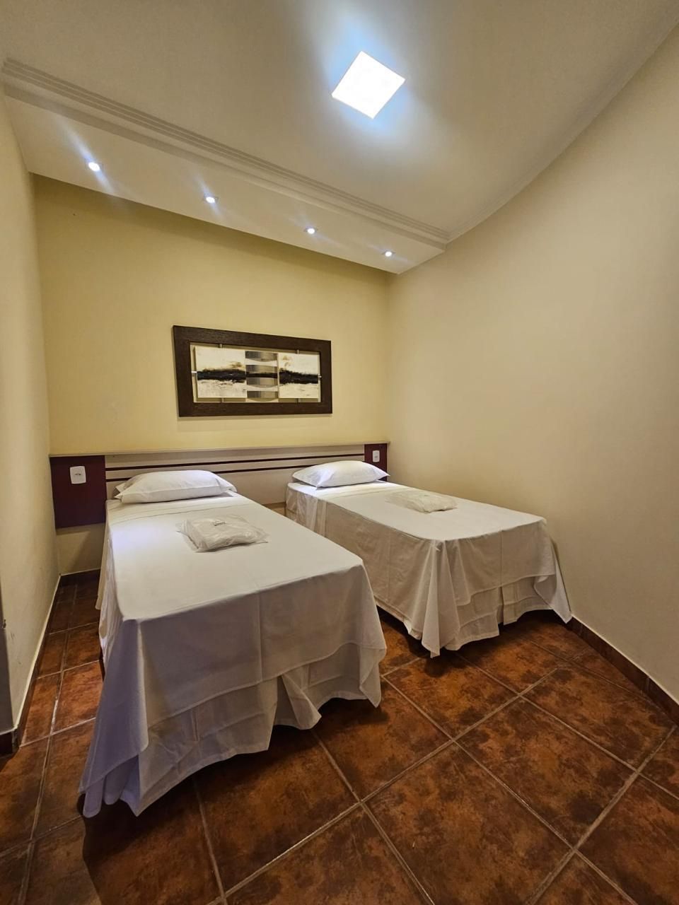 Ein Hotelzimmer mit zwei Einzelbetten, einer Deckenleuchte und einem gerahmten abstrakten Gemälde an der Wand.