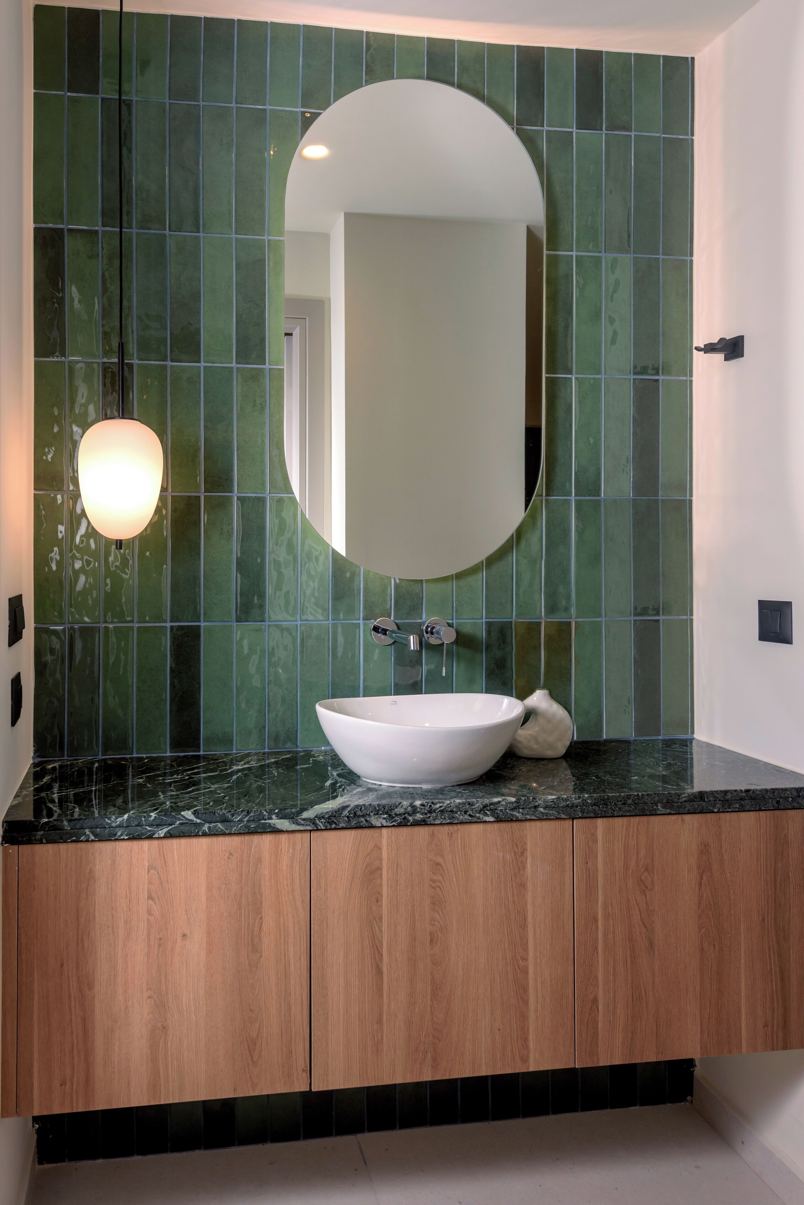 A bathroom with a white sink, a round mirror, and green tiled walls.
