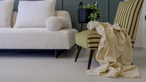 Uma sala de estar com um sofá, uma poltrona listrada, uma pequena mesa lateral preta com uma planta e um cobertor branco na poltrona.