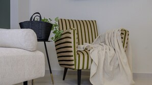 Quarto com sofá, poltrona listrada, mesinha com cesta e planta em vaso.