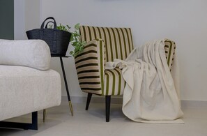 Ein Zimmer mit einer Couch, einem gestreiften Sessel, einem kleinen Tisch mit einem Korb und einer Topfpflanze.