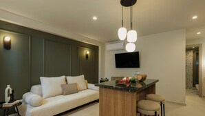 Uma sala moderna com um sofá, uma ilha de madeira com banquetas, uma televisão de tela plana na parede e uma pequena mesa lateral com objetos decorativos.