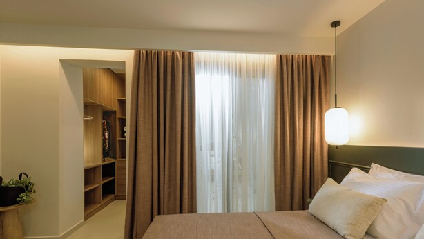 Quarto de hotel com cama, mesa de cabeceira, luminária, armário e janela com cortinas.
