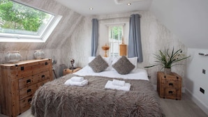 A bedroom with a large window, a bed with a fluffy blanket, wooden furniture, and a potted plant. - Cameron North Lodge on Loch Lomond (Argyll and Bute Council)