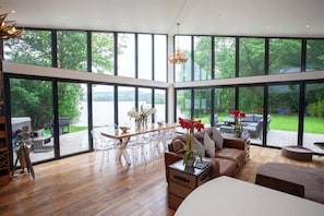 Amplia sala de estar con grandes ventanales, suelo de madera y vista a un lago.