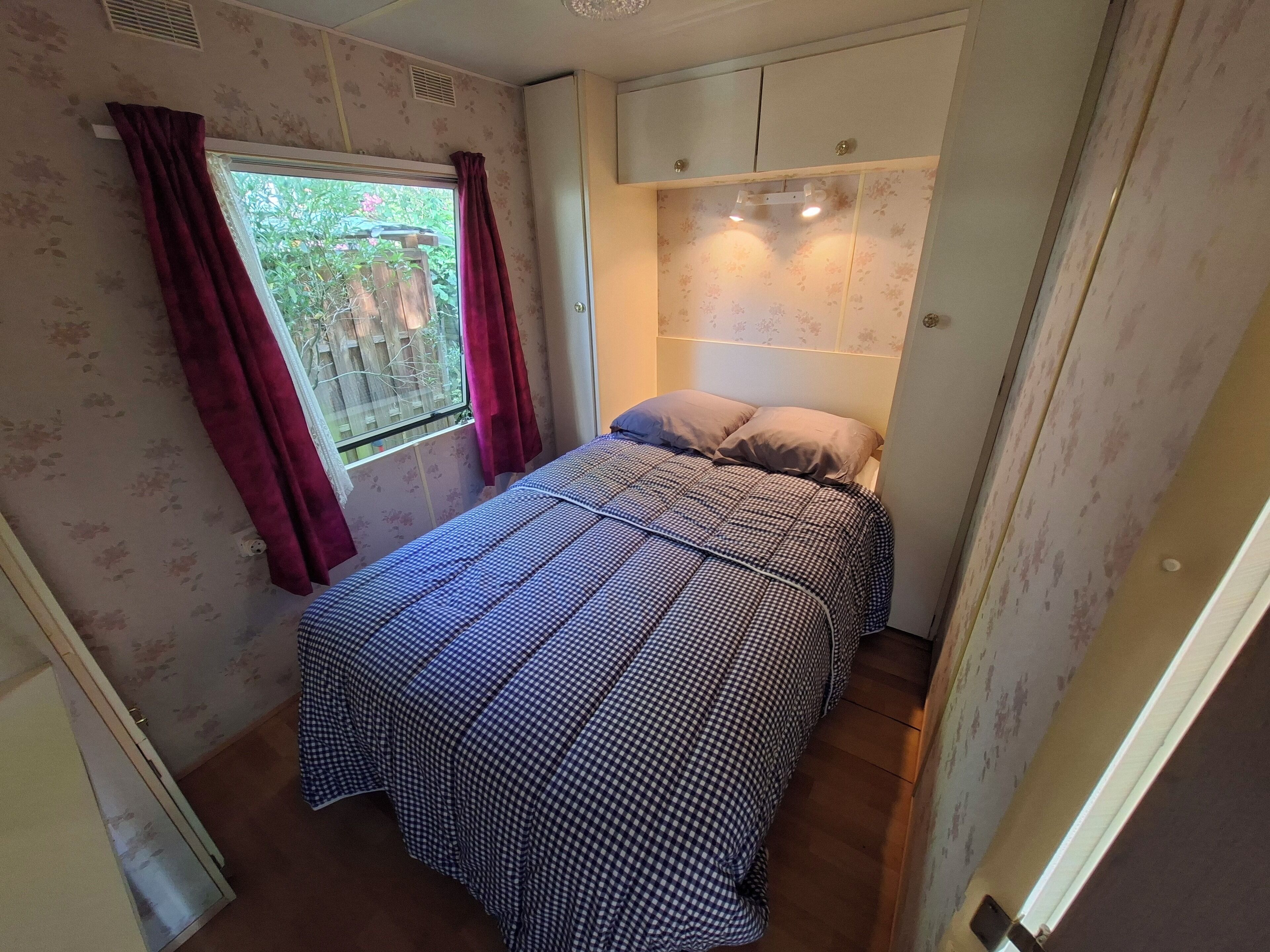 Une petite chambre à coucher avec un lit, une fenêtre avec des rideaux, un radiateur et une porte.