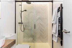 A modern bathroom with a glass-enclosed shower, a white sink, and a towel rack with towels. - An architect-style one-bedroom in Salesas, Chueca's most elegant corner, with pocket doors that close off a grand backlit bedroom and a calm, minimalist design. (MADRID)