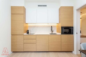 A modern kitchen with wooden cabinets, a white countertop, a built-in microwave, and a sink. - An architect-style one-bedroom in Salesas, Chueca's most elegant corner, with pocket doors that close off a grand backlit bedroom and a calm, minimalist design. (MADRID)