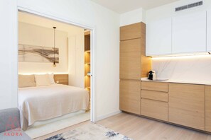 Quarto moderno com cama, mesa de cabeceira e criado-mudo. Possui um guarda-roupa embutido com espelho e uma pequena prateleira.