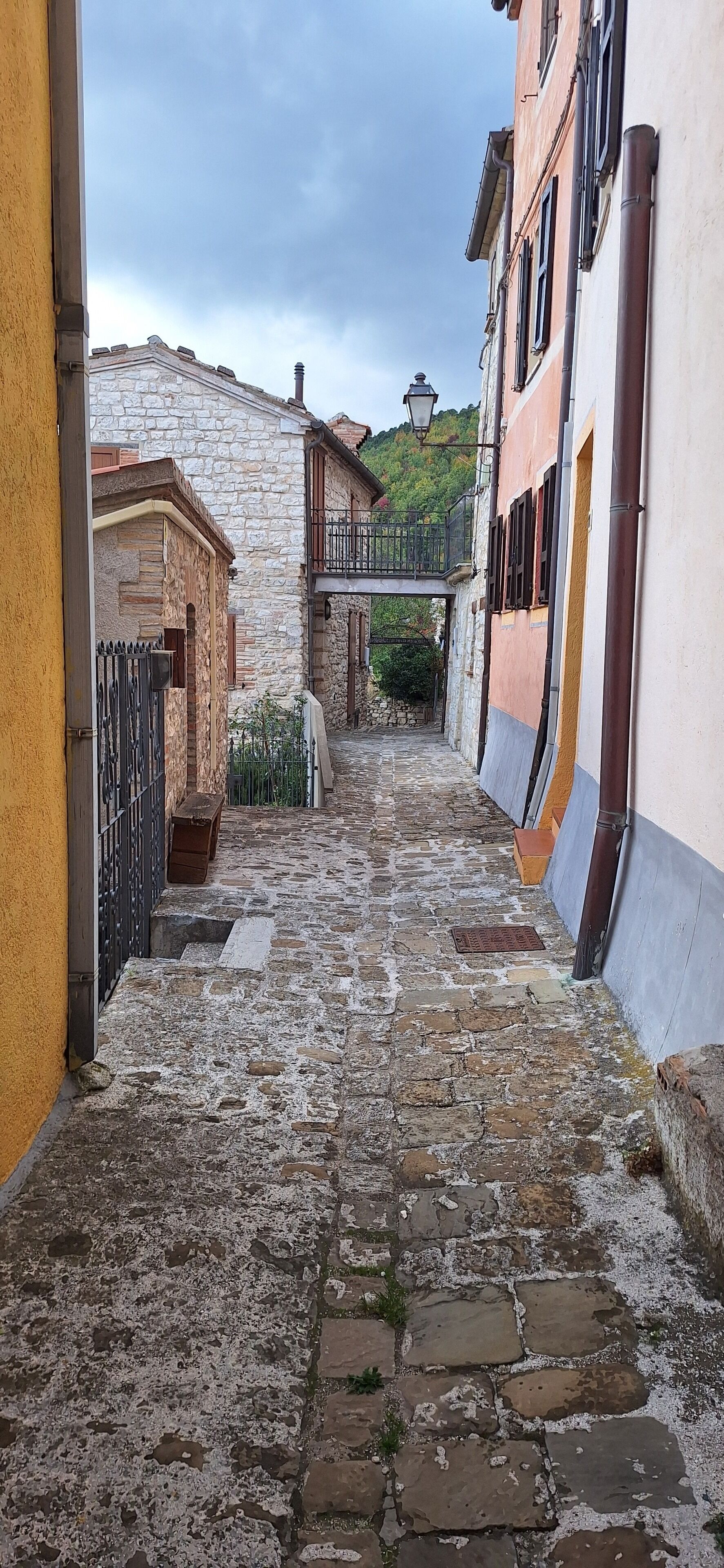 A narrow cobblestone street flanked by stone buildings with balconies and a small bridge overhead.