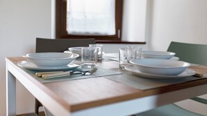 Een eettafel gedekt met witte borden, kommen en glazen, met een raam op de achtergrond.