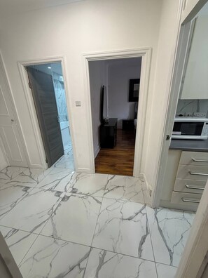 A hallway with marble flooring leading to a room with a wooden floor. There is a microwave and a small table in the room. - Charming Central Apartment Steps From Hyde Park (London)
