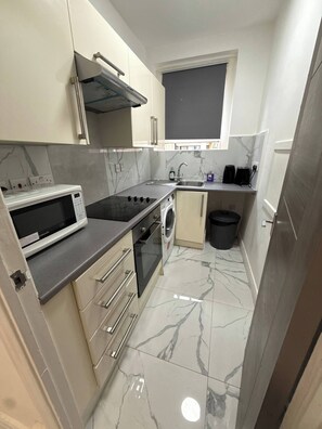 A compact kitchen with a microwave, stove, oven, sink, and a small window. - Charming Central Apartment Steps From Hyde Park (London)