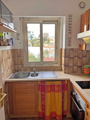 A kitchen with a double sink, wooden cabinets, a window with a view, and a sign reading "BON APPETIT". - Les Camelias – Bright One-Bedroom Apartment with Terrace and Garage (Antibes)