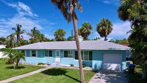 A single-story house with a blue exterior, a front garage, and a well-maintained lawn. - Sweet Slice of Old Florida Charm with modern amenities, large yard & beach gear (Holmes Beach)