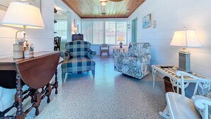 A cozy living room with a wooden ceiling, a plaid armchair, a floral sofa, and a wooden table. - Sweet Slice of Old Florida Charm with modern amenities, large yard & beach gear (Holmes Beach)