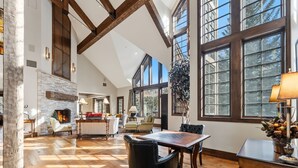 Uma sala de estar espaçosa com lareira, piso de madeira e grandes janelas com vista para o exterior.