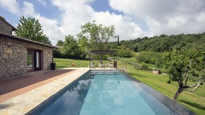 A rectangular swimming pool with a stone deck, a pergola, and a stone house with a tiled roof. - Casa Pernice - Stylish Chianti Retreat with Pool & Vineyard Views (Gaiole in Chianti)