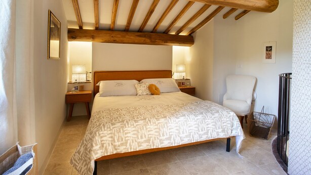 A bedroom with a wooden ceiling, a bed with patterned bedding, bedside lamps, a chair, and a small table. - Casa Pernice - Stylish Chianti Retreat with Pool & Vineyard Views (Gaiole in Chianti)