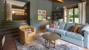A modern living room with a sofa, armchair, and coffee table. There is a staircase leading to a kitchen area. - Casa Pernice - Stylish Chianti Retreat with Pool & Vineyard Views (Gaiole in Chianti)