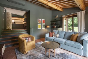 Una sala de estar moderna con sofá, sillón y una mesa de centro. Se ve una escalera que lleva a una zona de cocina.