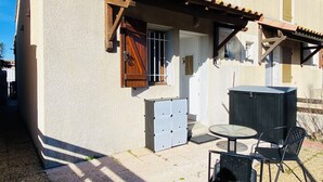 Ein Gebäude mit einer Terrasse, die einen Tisch und Stühle, eine Holztür und eine kleine Gartenhütte beinhaltet.