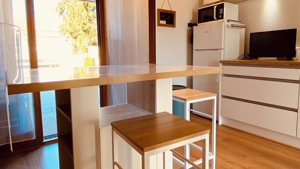 Eine kompakte Küche mit Mikrowelle, Kühlschrank und einer kleinen Essecke mit Holztisch und Barhocker.