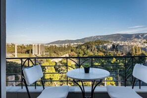 A balcony with two white chairs and a small round table, overlooking a cityscape with buildings and greenery. - Acropolis Elegant Penthouse, Apartment (Athens)