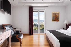 A hotel room with a bed, a desk, a chair, a TV, a painting, and a view of the city. - Acropolis Elegant Penthouse, Apartment (Athens)