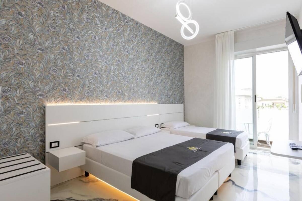A modern hotel room with a large bed, bedside tables, a small desk, and a view of the outdoors.