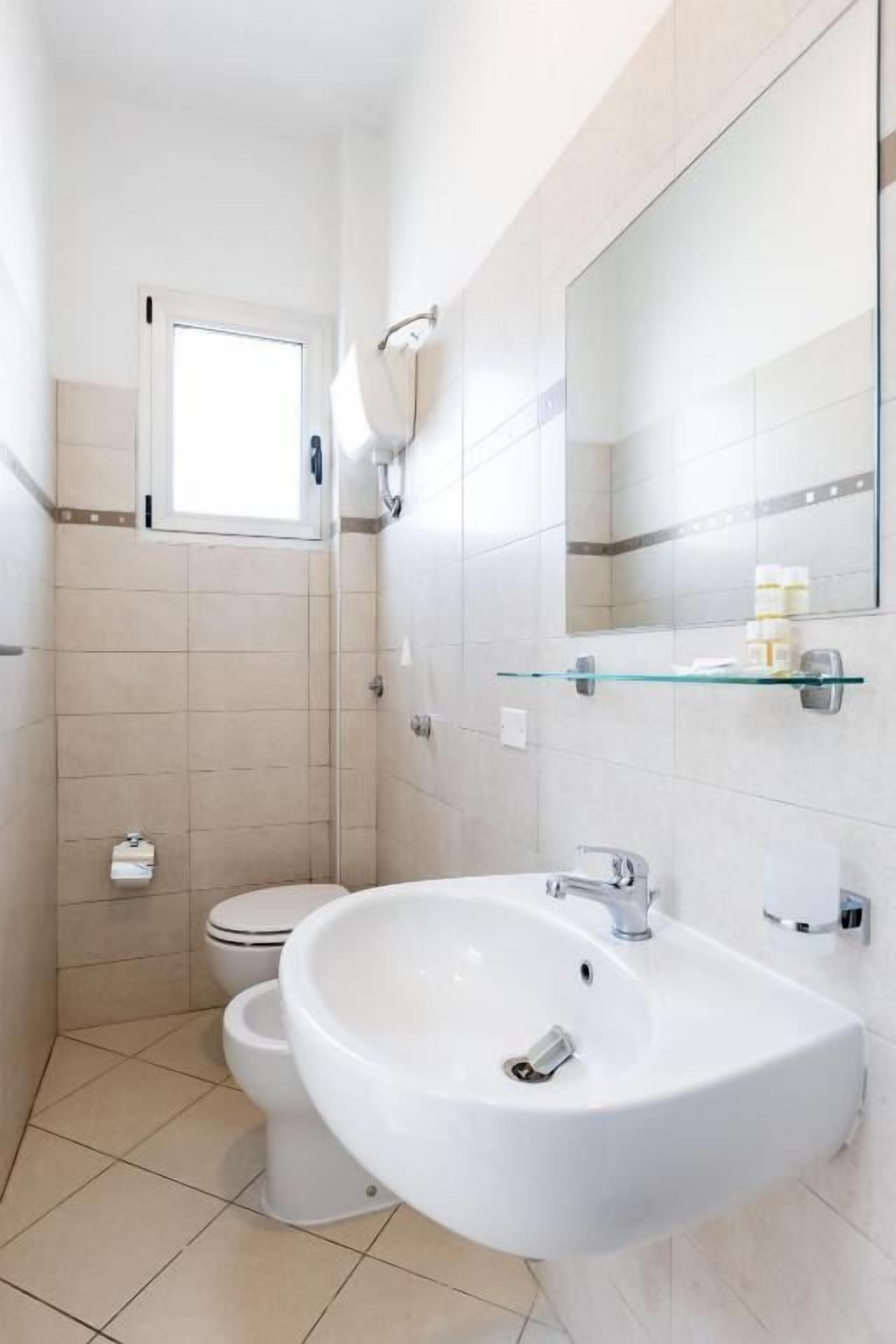 Ein modernes Badezimmer mit einem weißen Waschbecken, einer Glasablage, einem Spiegel und einer Toilette.