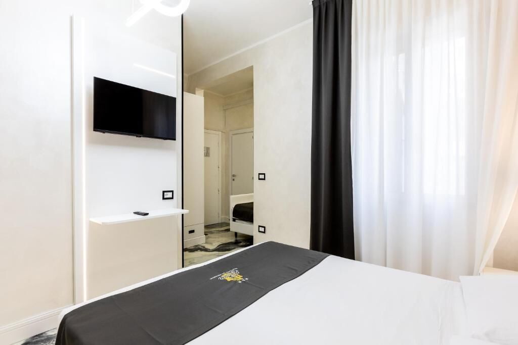 A hotel room with a bed, a TV mounted on the wall, and a bathroom visible through an open door.