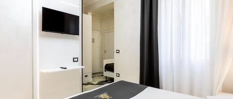 A hotel room with a bed, a TV mounted on the wall, and a bathroom visible through an open door.