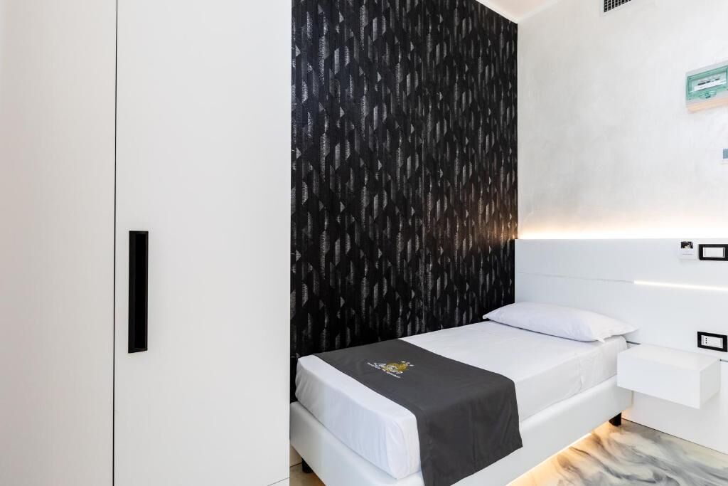 A modern hotel room with a bed, a white nightstand, and a black patterned wall.