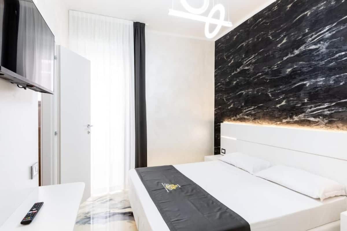 A modern hotel room with a bed, a TV mounted on the wall, and a large window with curtains.