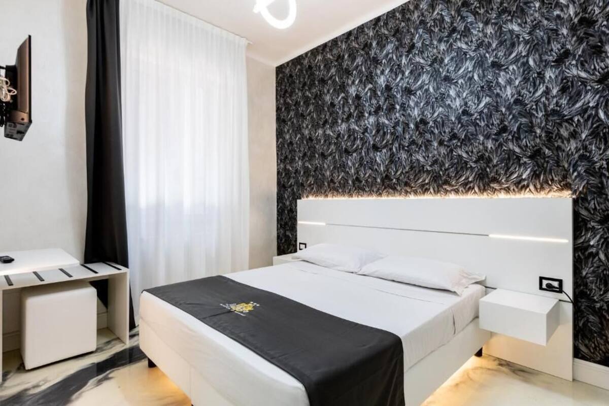 A modern hotel room with a large bed, a bedside table, a desk, and a wall-mounted TV.