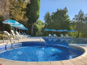 A swimming pool with tiled blue floor, white lounge chairs, and blue umbrellas. - Park Hotel Rusalka (Varna)