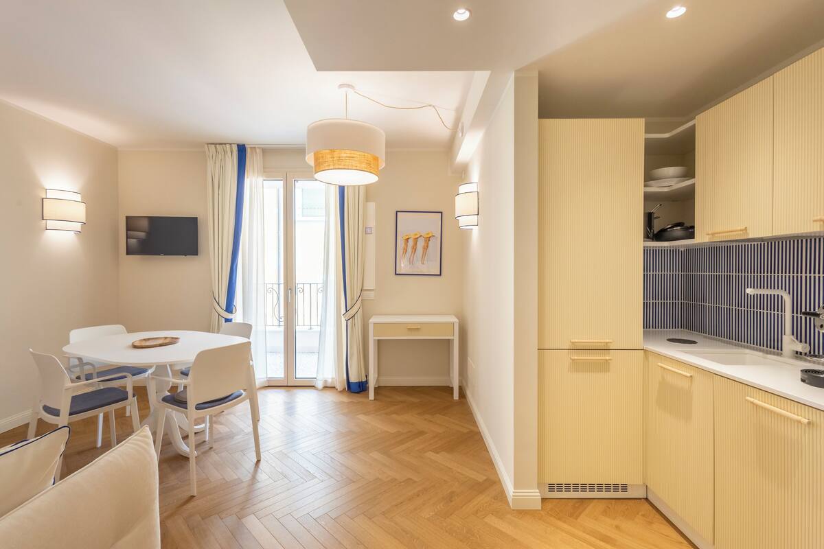A modern kitchen with white cabinets, a dining area with a white table and chairs, and a large window with curtains.