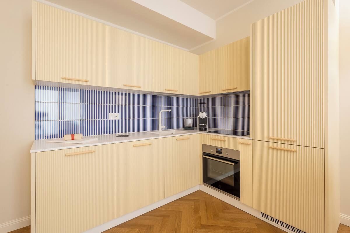 A modern kitchen with light-colored cabinetry, a stainless steel oven, and a blue-tiled backsplash.