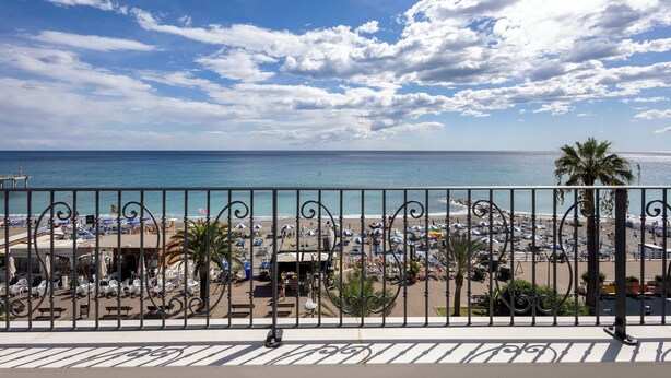 A beach view with a balcony railing, beach umbrellas, and palm trees. - A'mare Luxury Apartments (Pietra Ligure)