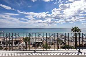 A beach view with a balcony railing, beach umbrellas, and palm trees. - A'mare Luxury Apartments (Pietra Ligure)