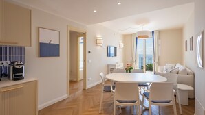 A modern living room with a round dining table, white chairs, a sofa, and a TV on the wall. - A'mare Luxury Apartments (Pietra Ligure)