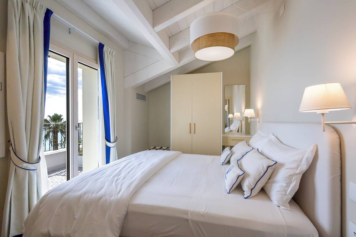 A hotel room with a bed, a wardrobe, a balcony with curtains, and a ceiling light.
