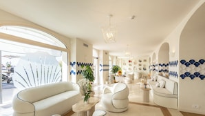 A spacious, well-lit hotel lobby with modern furniture, a large window, and decorative wall panels. - A'mare Luxury Apartments (Pietra Ligure)