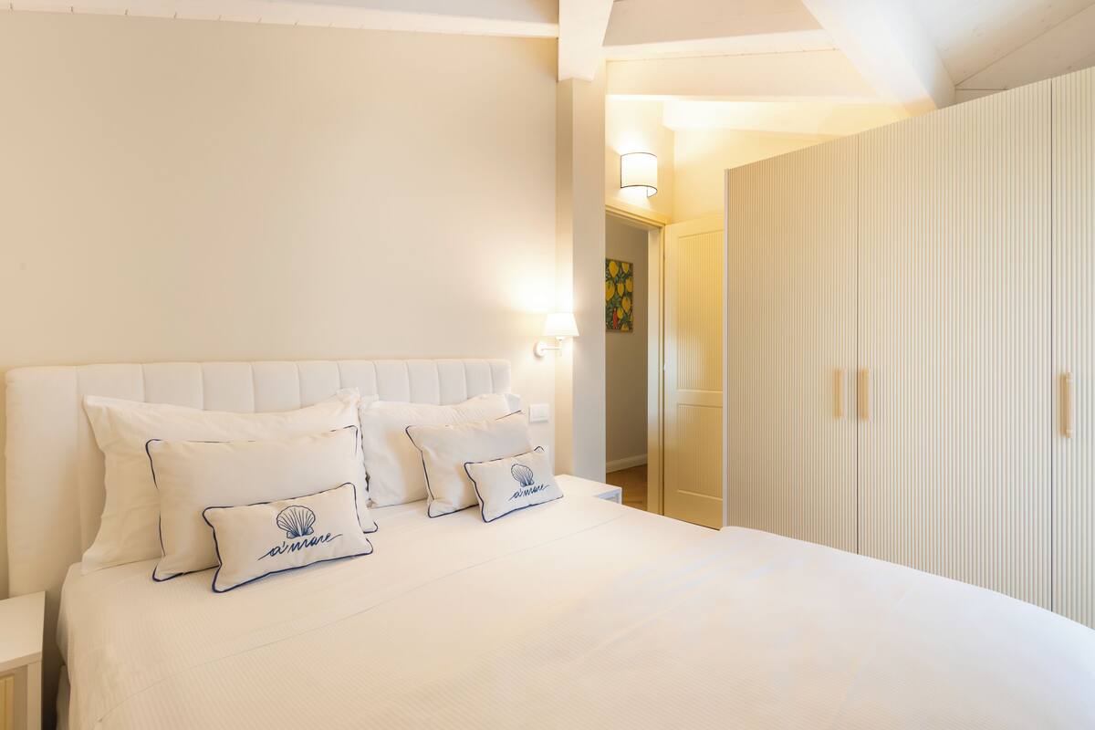 A neatly made bed with two pillows, a white headboard, and a bedside lamp.
