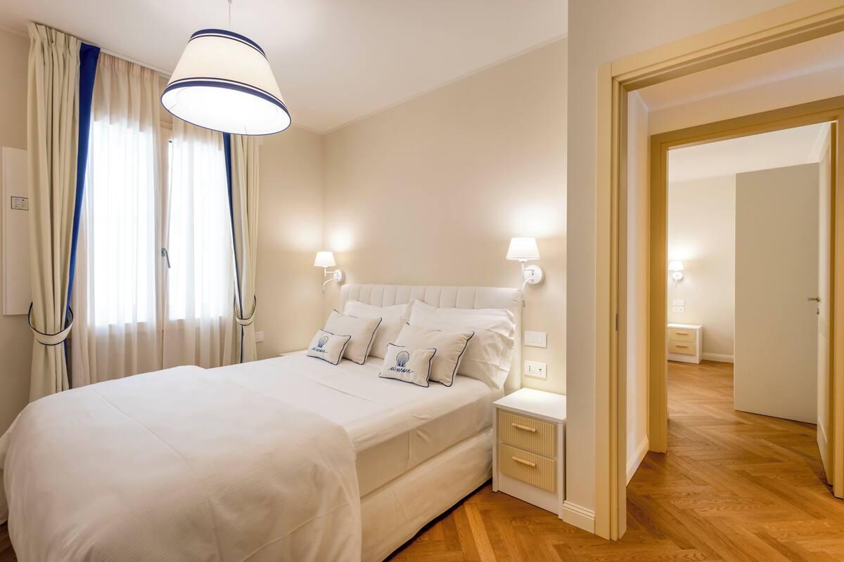 A neatly arranged bedroom with a large bed, bedside tables, and a door leading to another room.